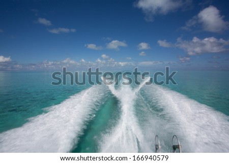 Wave of power boat creates long white wave pattern in turquoise blue tropical waters