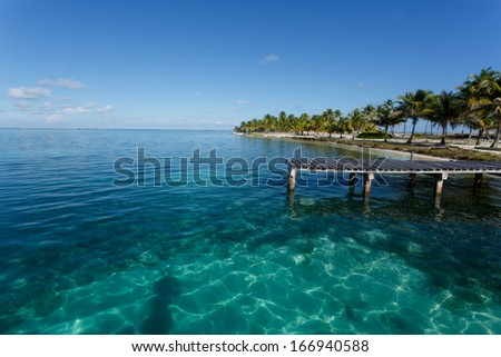 Dock on tropical island loaded with palm trees highlight pattern of sunlight in beautiful turquoise waters of the Caribbean