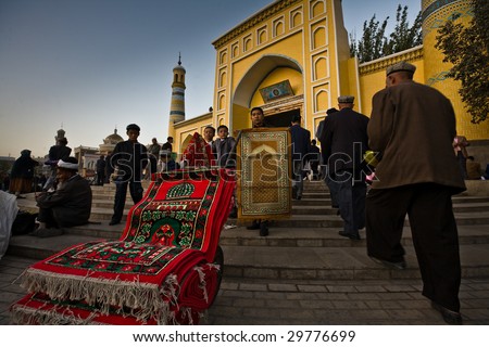 KASHGAR, CHINA- OCT 2: Two Uyghur boys and a man sell colorful prayer carpets on the steps of Id Kah Mosque during Ramadan  month services October 2, 2008 in Kashgar,  Xinjiang province western China.