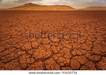 Cracked pattern of dry lake bed and sand dunes in Sahara Desert Morocco