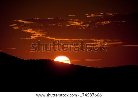 Sun goes down behind a hill above the sea level with clouds