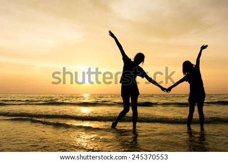 Silhouette of two women wave hand in sunset sky at the sea. Happiness concept.