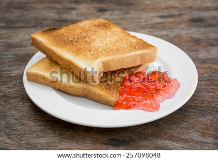 Toast bread with jam on plate on wooden table background.