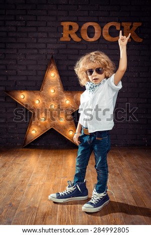 Little Boy Rock Star Giving The Rock And Roll Sign On Brick Wall Background