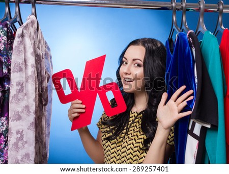 Happy Woman Holding Percent Sign At The Clothing Rack With Dresses On Blue Background