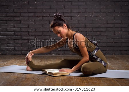 Beautiful Girl Doing Yoga Exercises And Read Book On Brick Wall Background