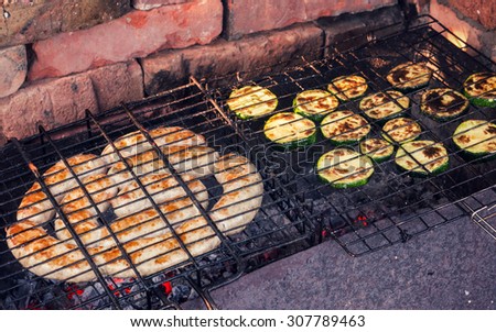Sausages and zucchini cut into slices cooking on an outdoor grill.