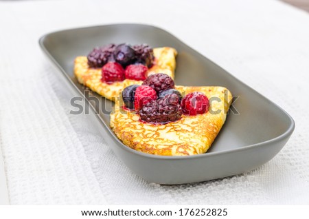 Crepes with wild berries on a grey plate on a white towel. Shallow depth of field.