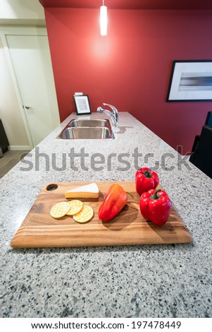 Modern red kitchen interior with a cutting board with cheese, crackers, and red peppers.
