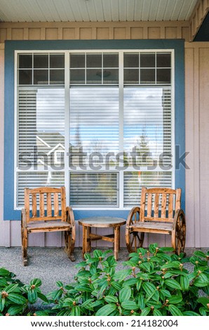 Front of a rustic house with a patio: two chairs and a table. Home exterior.