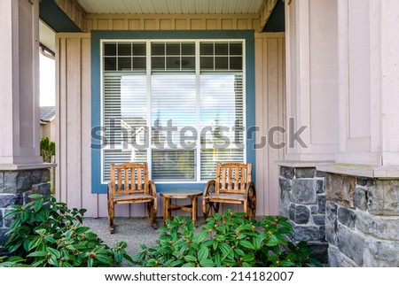 Front of a rustic house with a patio: two chairs and a table. Home exterior.