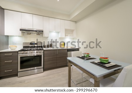 Modern, bright, clean kitchen interior with stainless steel appliances and dinner table in a luxury apartment.