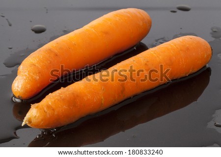 Two carrots on a wet black background.
