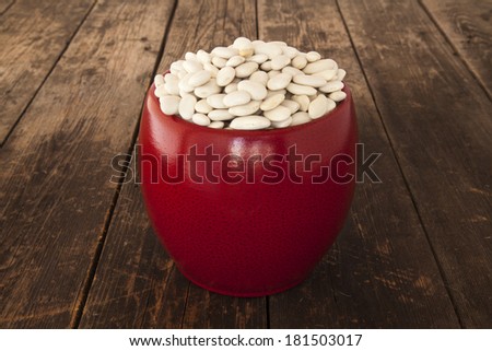 White beans in a red bowl on wooden background.