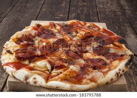 Delicious peperoni pizza pie, with melted cheese and ketchup sauce, shot centered on a warm wooden surface.