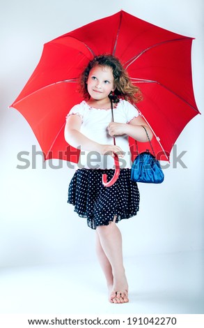Pretty little girl posing with red umbrella in studio.