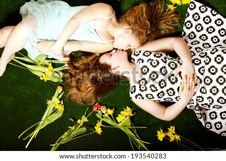 Two pretty young sisters lying over colorful flowers, kissing. Children\'s day. Happy family.