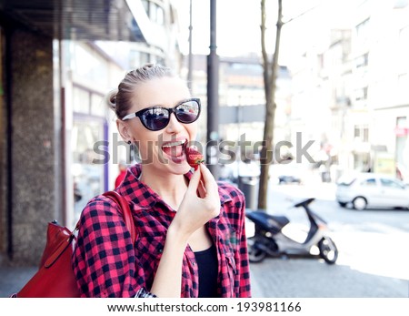 Young beautiful woman eating fresh strawberry. Street photo. Summer time.