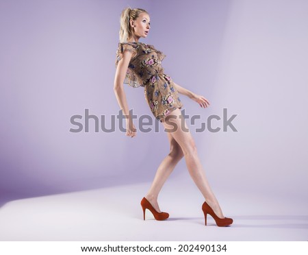 Fashionable blonde woman posing in studio, looking away. Girl with long slim legs.