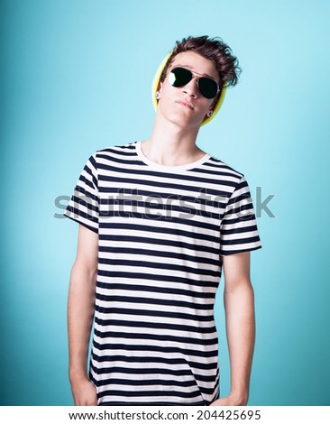Young fashionable handsome guy posing wearing sunglasses. Studio photo. Blue background.