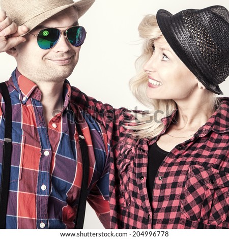 Beautiful blonde young woman posing with handsome man wearing hat, smiling.