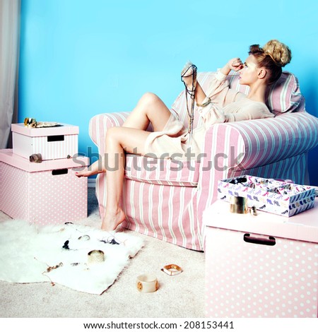 Attractive sad blonde beauty sitting in room with a lot of jewelry, thinking.