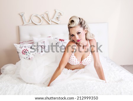 Romantic beautiful blonde woman relaxing in big bed, leisure time. Love lettering on the wall.