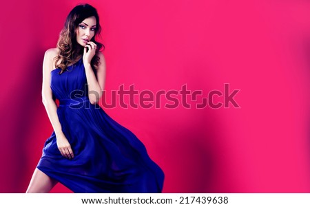 Sensual brunette beautiful woman posing in fluttering long dress. Pink background. Girl looking at camera