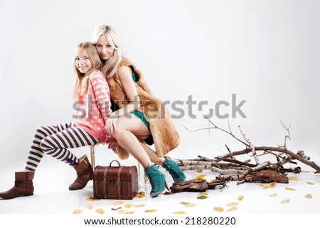 Fashionable beautiful blonde woman posing with her pretty daughter, looking at camera. Autumn photo