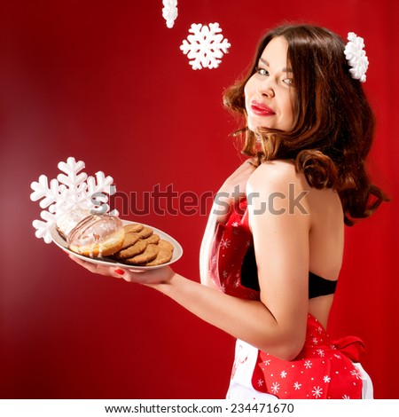 Beautiful brunette smiling woman posing in kitchen apron over snowflakes holding sweet cookies