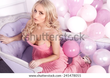 Romantic beautiful blonde woman in pink dress posing over balloons, looking at camera.