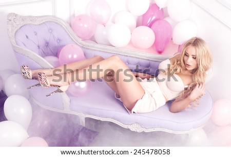 Sensual beautiful blonde woman lying over balloons, relaxing. Girl with long slim legs.