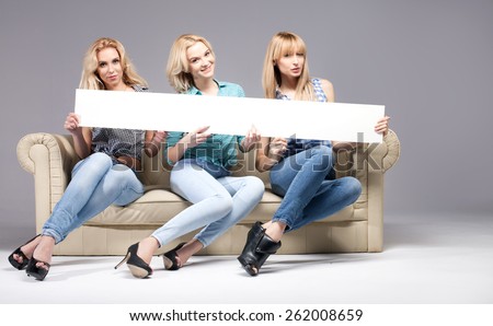 Group of beautiful blonde woman holding empty board, smiling and looking at camera. Studio shot.