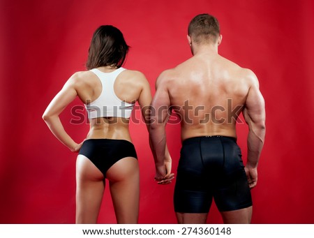 Muscular man and woman posing over red background. Back view.