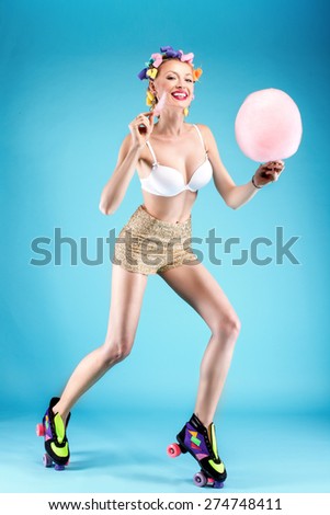 Happy beautiful young woman eating candy cotton. Blue background. Smiling girl having fun. Summer photo.
