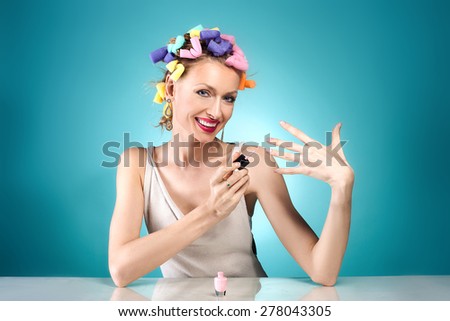Beauty portrait of attractive woman posing with nail polish and with curlers on her head. Blue background.