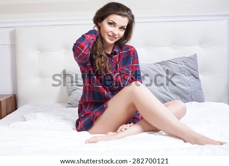 Beautiful young brunette woman relaxing in bedroom, smiling. Indoor photo.