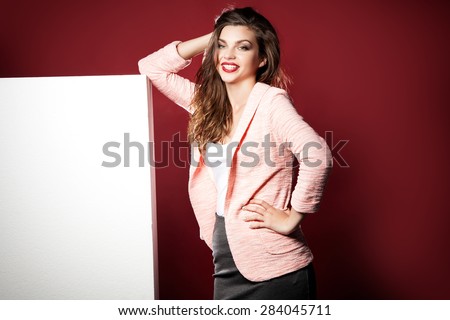 Young beautiful brunette woman posing with empty white board, posing in studio. Girl looking at camera and smiling.