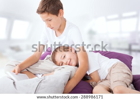 Little boy lying, listening a story. Older brother reading a book. Family photo.