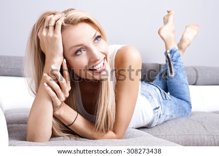 Beautiful smiling young blonde woman lying on the couch, relaxing at home. Girl looking at camera.