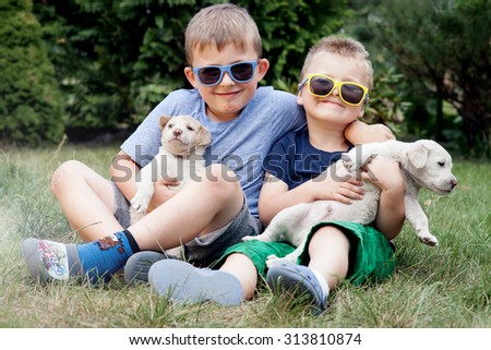 Two little brothers playing outdoor with puppies, smiling. Summer day.