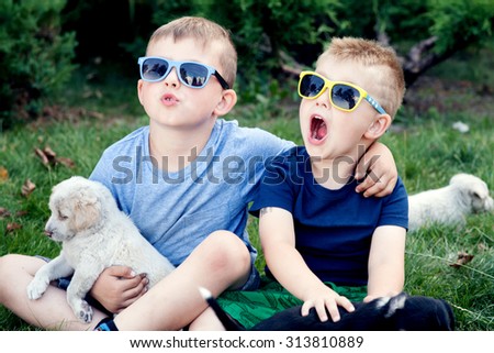 Two little brothers playing outdoor with puppies, smiling. Summer day.