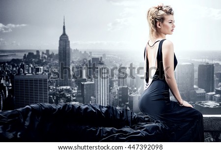 Stylish beautiful woman posing in black elegant dress. Skyline on background.