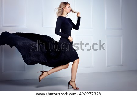 Beautiful elegant blonde woman posing in black maxi dress, looking at camera. Indoor shot.