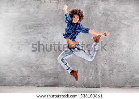 Young urban hip hop dancer jumping and dancing with grunge concrete wall background. Girl with afro hair.