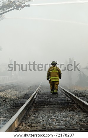DAYTON, OHIO - AUGUST 15: Firefighter walks railroad track through haze of smoke and water mist during an old, abandoned warehouse fire on August 15, 2008 in Dayton, Ohio, USA.
