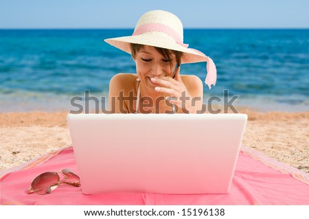 Smiling girl wearing bikini and straw hat using laptop at the sea