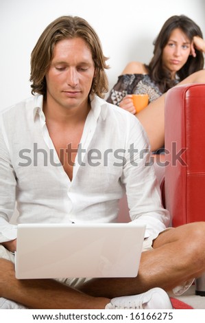 Young couple at home, she is sitting on the sofa and he works with laptop