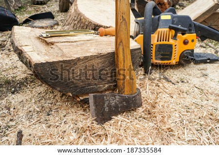 Wood tools - axe,  chainsaw file  and chainsaw in the background outdoor. focus on axe and wooden log