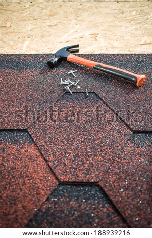 Asphalt shingles on a roof of wood with hammer and nails. focus on nails and roof
